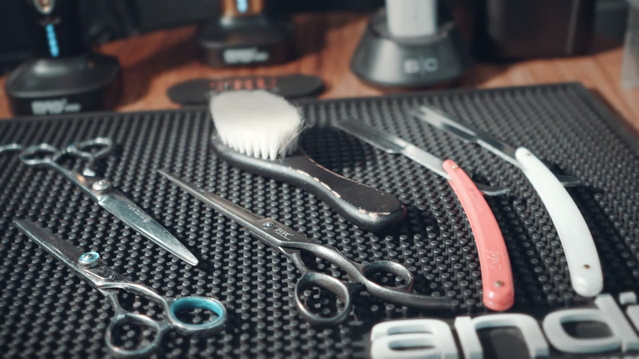 Scissors, razors and a brush laid out on a barber mat